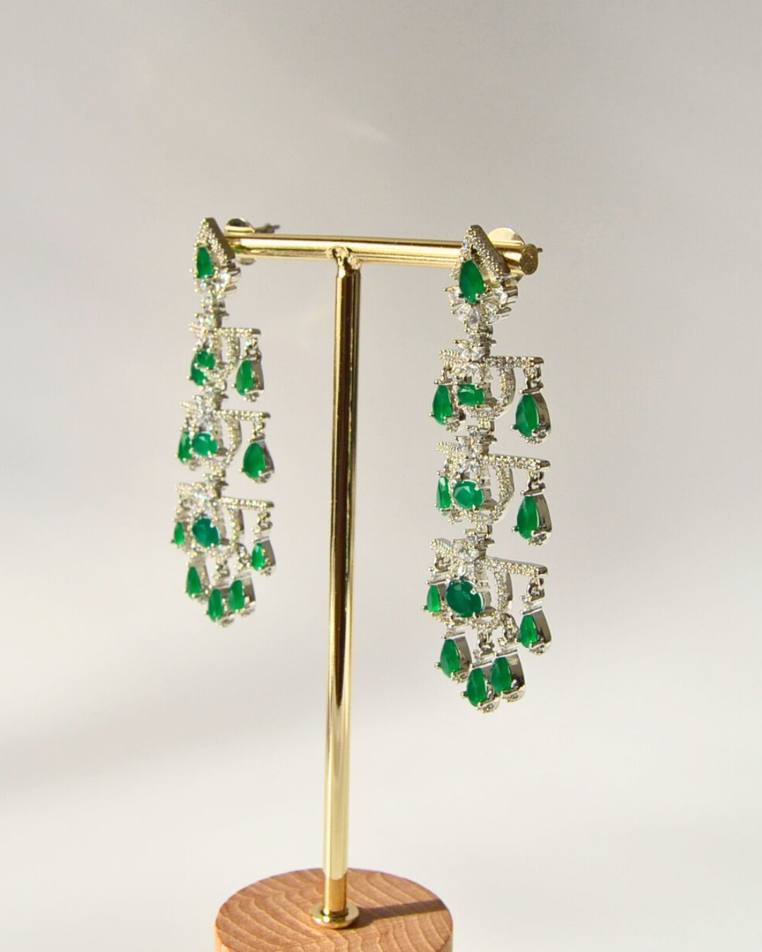 Pair of emerald earrings on a gold stand against a light gray background