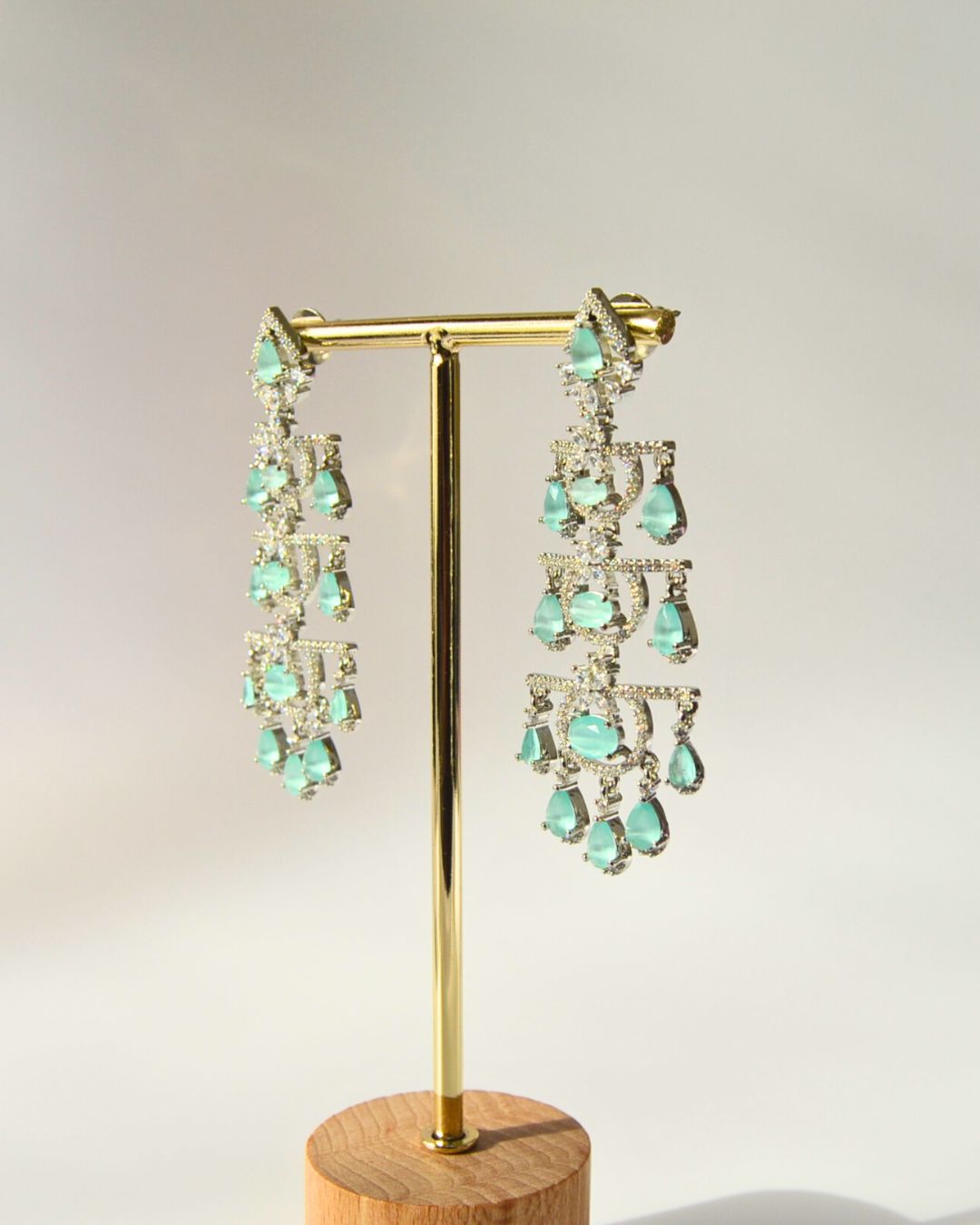 Pair of turquoise chandelier earrings on a gold stand with a wooden base.