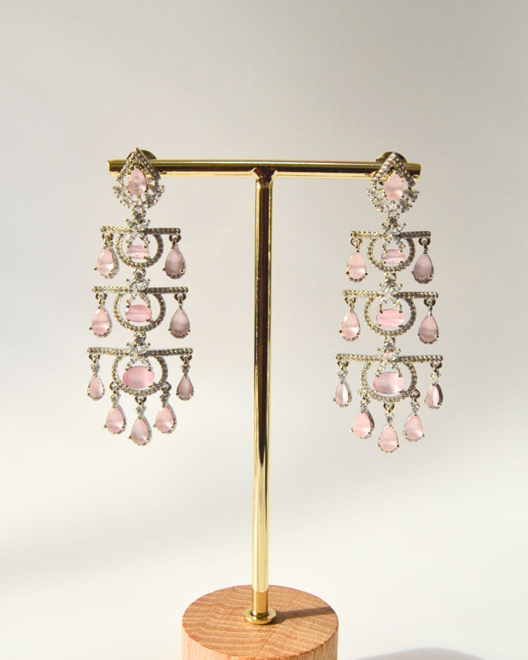 Pair of pink chandelier earrings on a gold and wooden stand against a light gray background