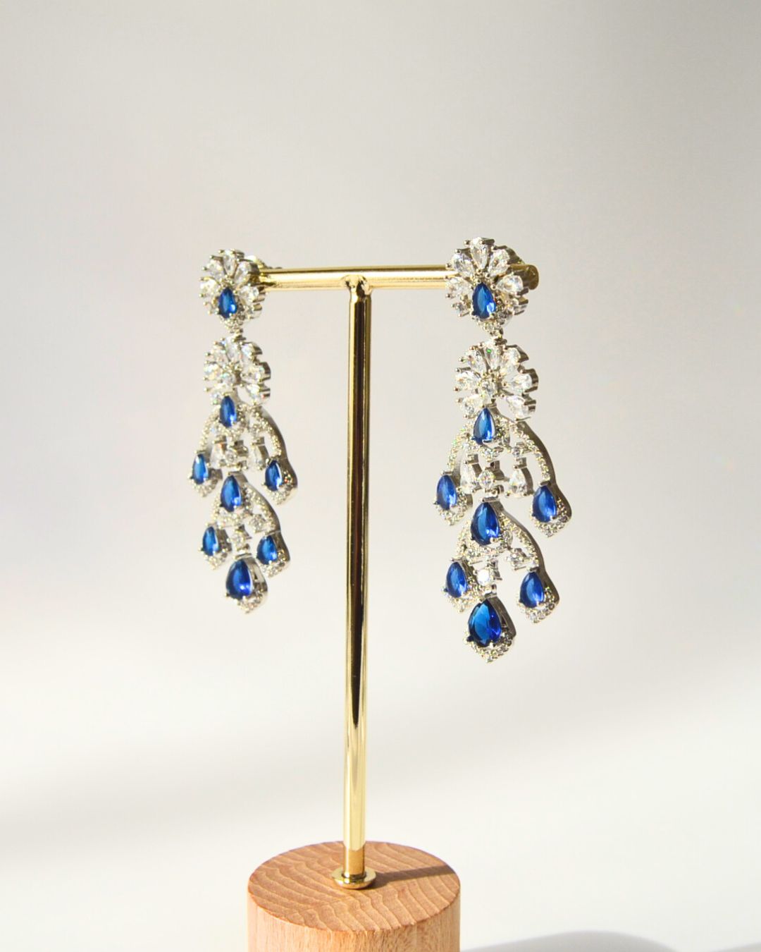 Pair of blue teardrop earrings on a gold stand with a wooden base against a white background