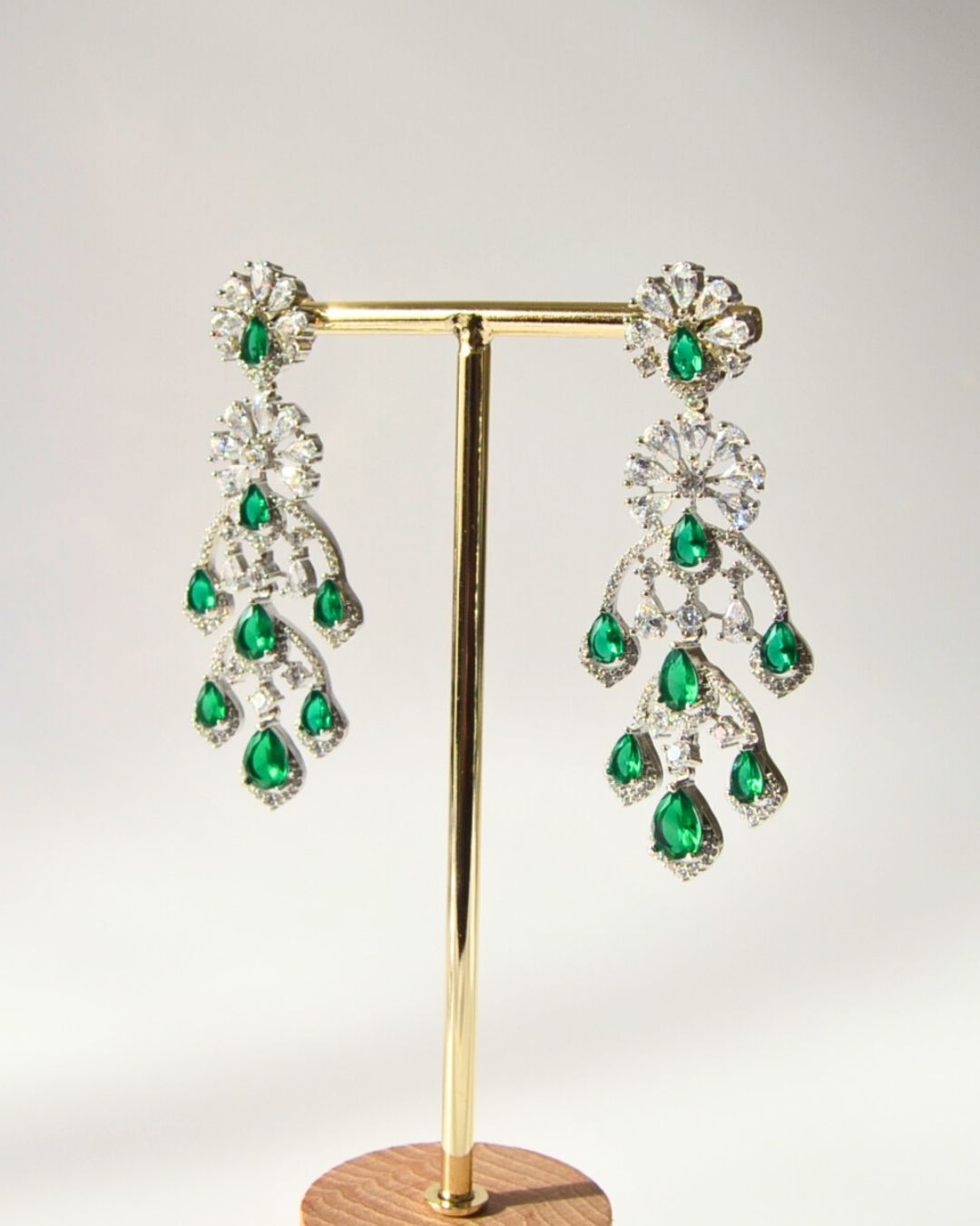 Pair of emerald green zircon chandelier earrings on a gold stand against a white background
