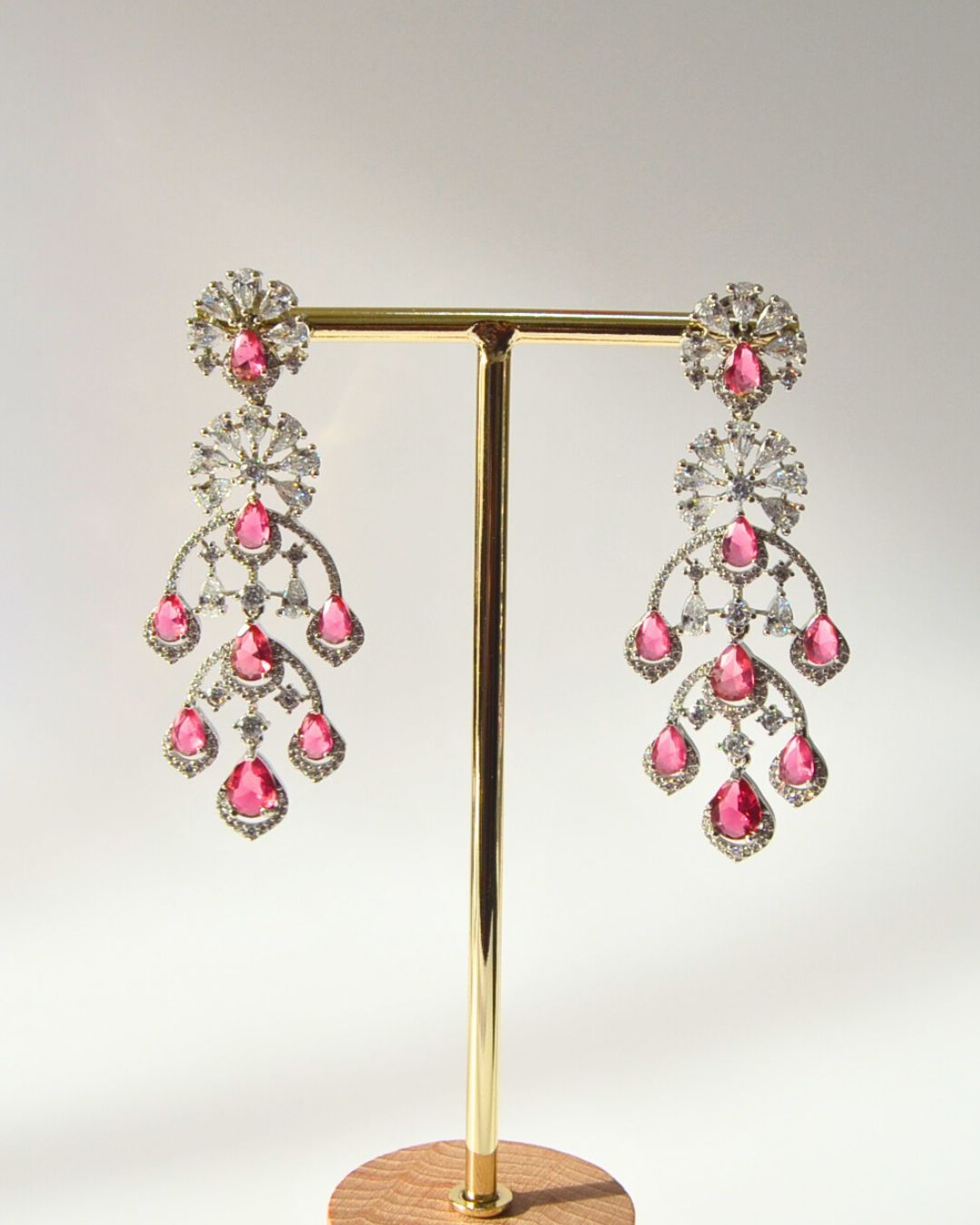 Magenta CZ Chandelier earrings on a gold stand against a white background
