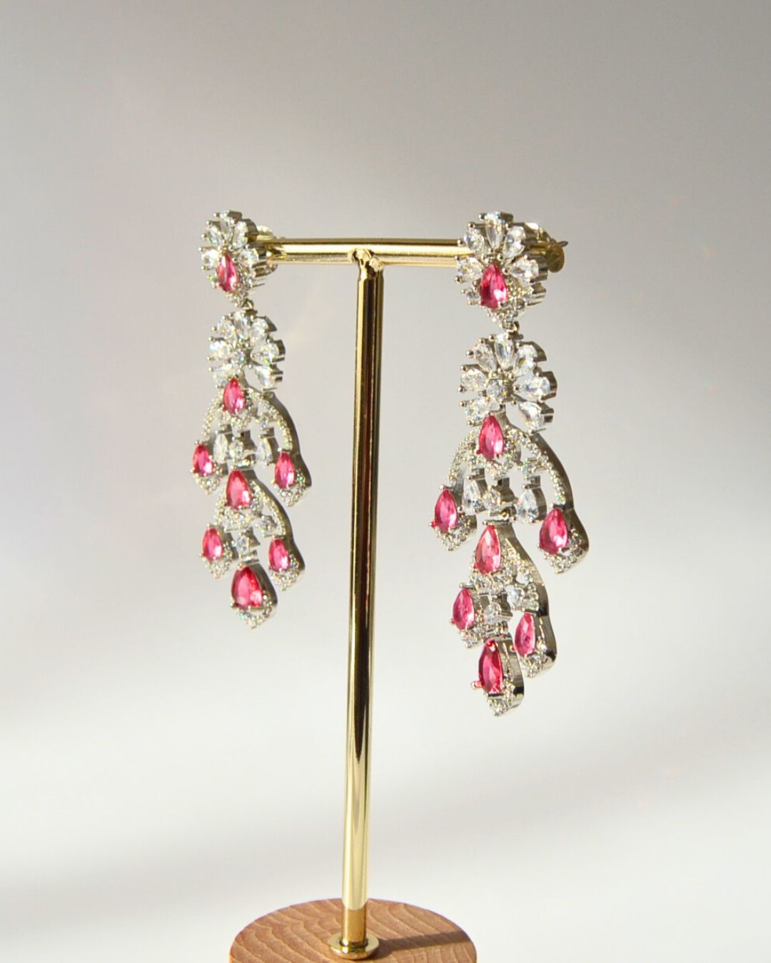 Chandelier earrings with Magenta cubic zirconia stones on a gold stand against a gray background