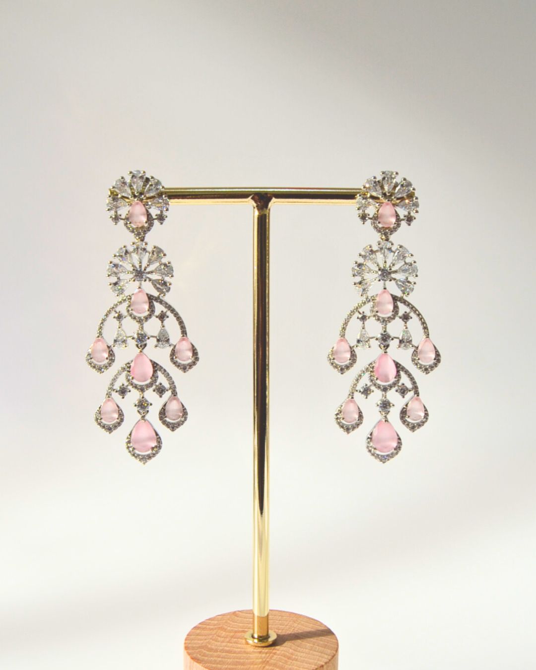 Pair of pink and clear crystal chandelier earrings on a gold stand against a light gray background