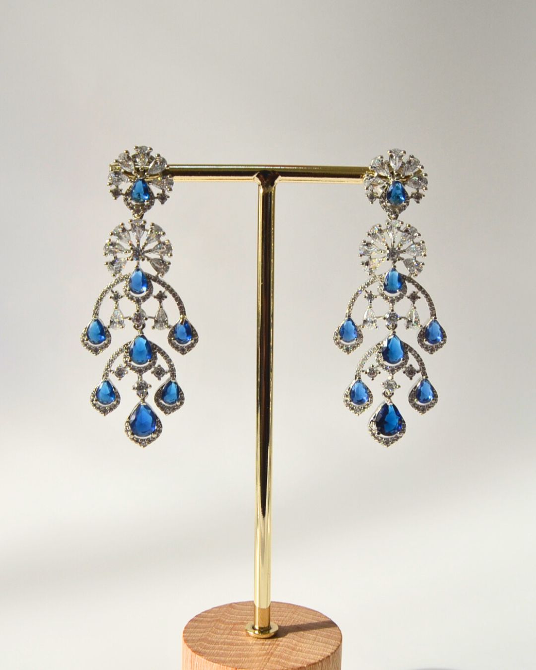Pair of chandelier earrings with blue gemstones on a gold stand against a gray background